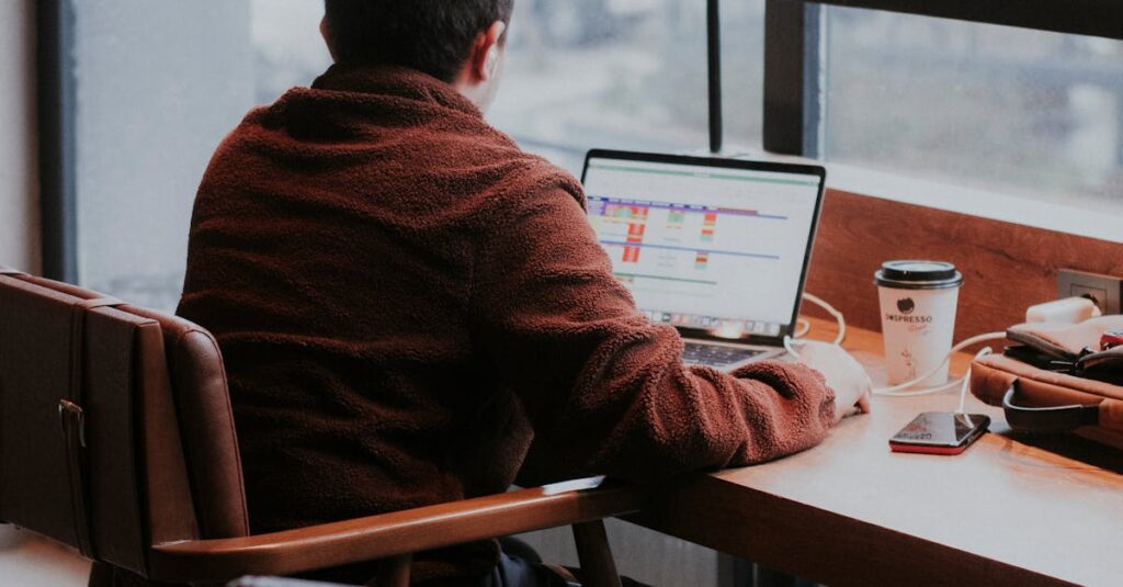 A man is working on a laptop at a café table, creating a warm, productive atmosphere.