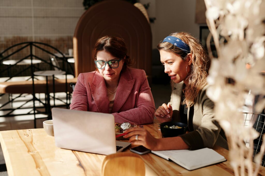 Two women working together on a laptop in a cozy café setting.