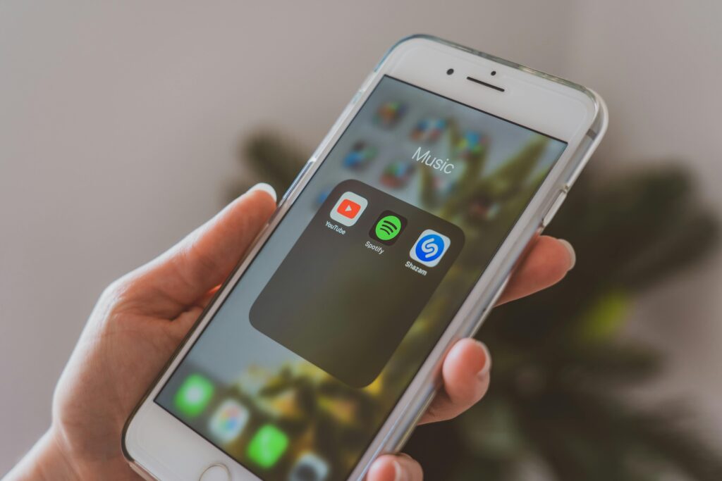 Hand holding a smartphone displaying popular music apps like Spotify and Shazam in a close-up shot.