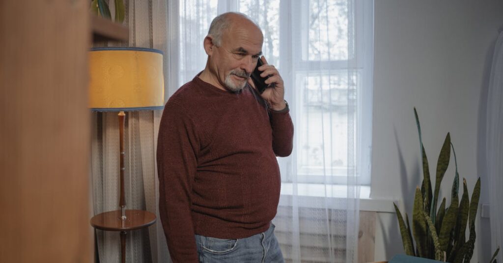 Senior man in brown sweater conversing on phone inside a warmly lit room.