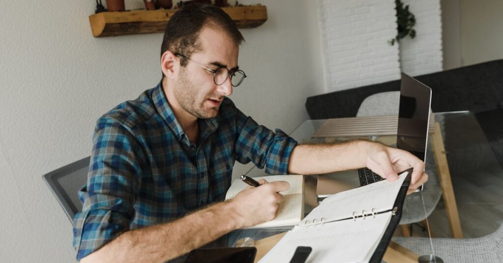 Caucasian male freelancer working from home with laptop, notebook, and pen.