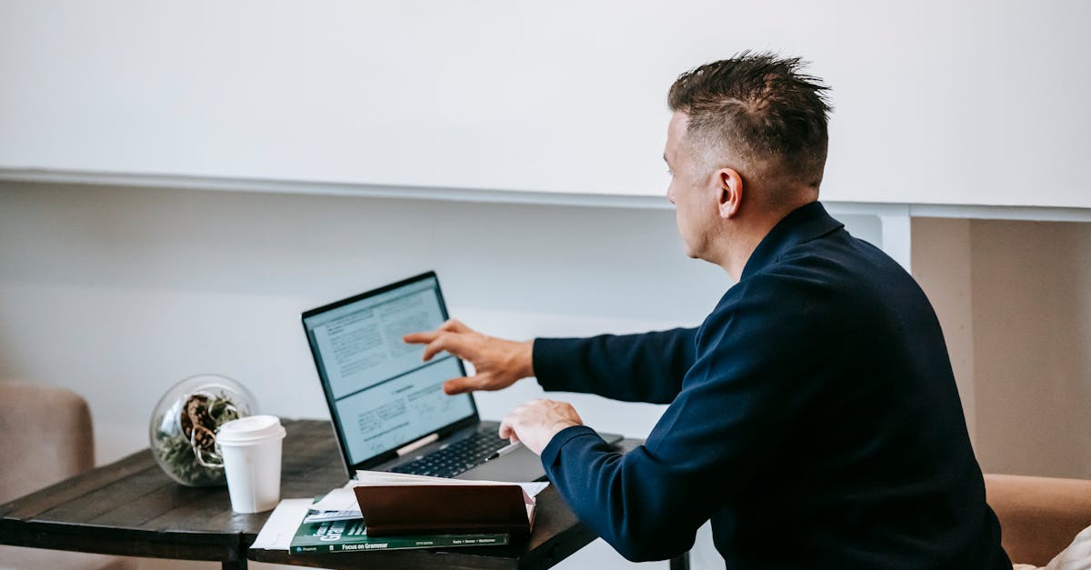 Man working remotely on a laptop in a cozy home office setting with coffee and documents.