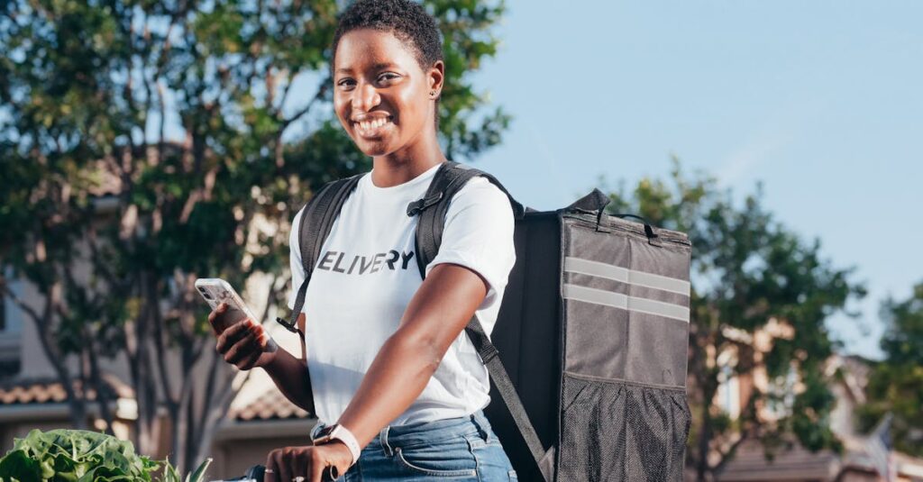 Smiling delivery woman using smartphone outdoors with a delivery bag.