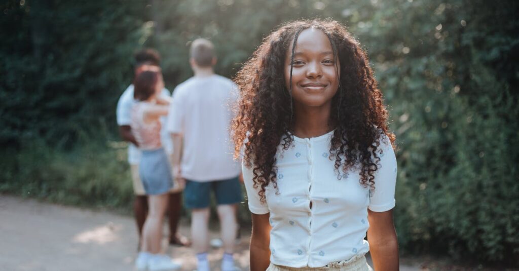 Teen girl smiling in a summer park, friends in background on a sunny day.