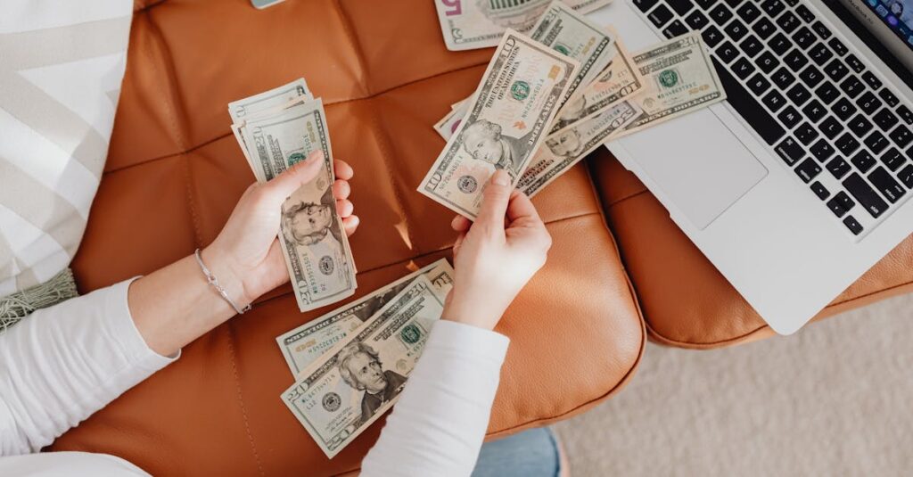 A person counts US dollar bills on a couch with a laptop, symbolizing financial planning.