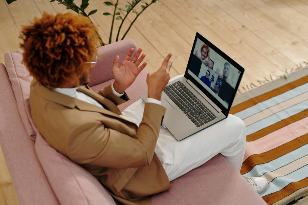 An adult man in a suit engages in a video call while sitting on a sofa indoors.