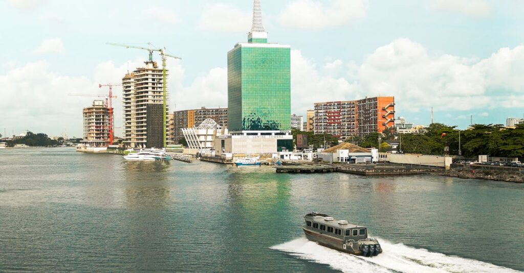 Scenic view of Lagos skyline featuring modern buildings and a motorboat in the lagoon under a bright sky.