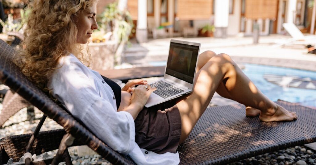 Woman with curly hair working on a laptop outdoors by the poolside, embracing remote work lifestyle.