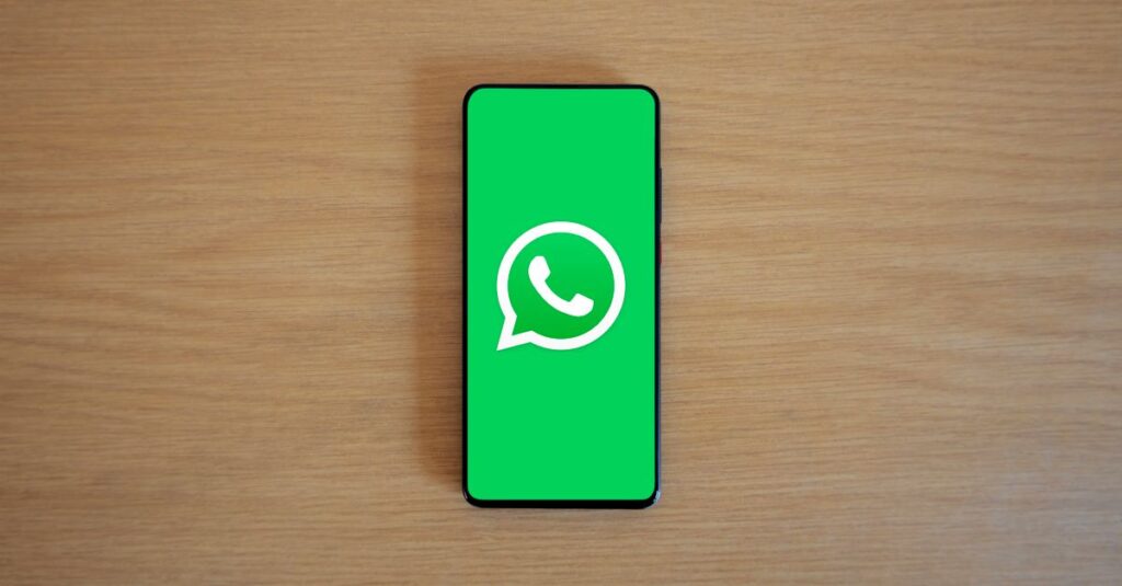 Top view of smartphone displaying WhatsApp logo on a wooden background, representing technology and communication.