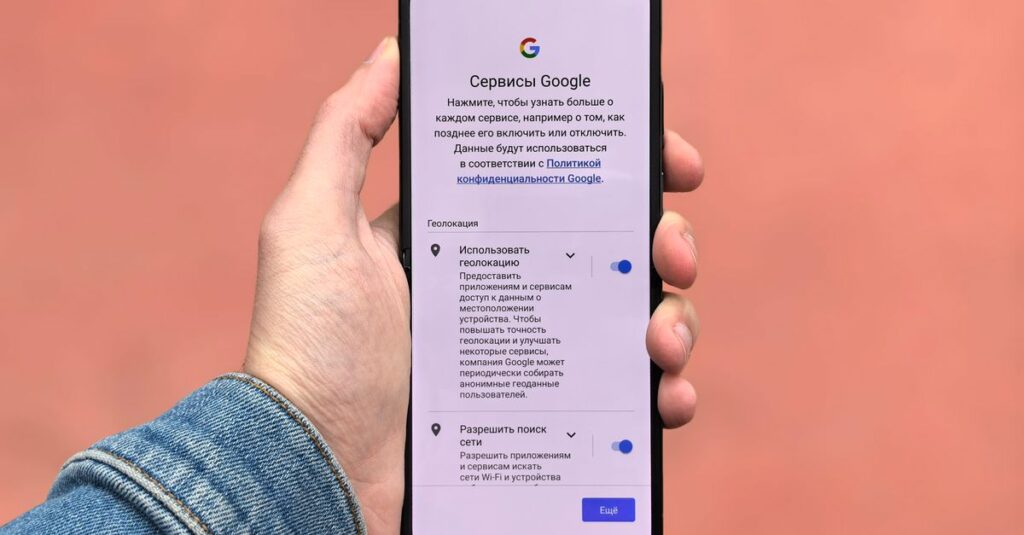 A person holding a smartphone displaying Google settings on a simple background.