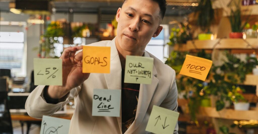 Young man brainstorming with sticky notes on glass wall in modern office setting.