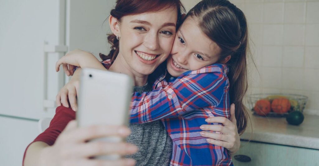 Smiling mother and daughter taking a selfie in a cozy indoor setting.